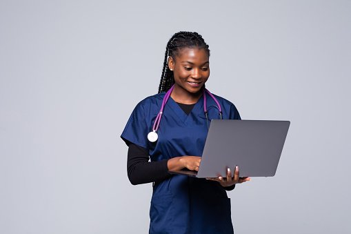 A clinician in scrubs working at a laptop