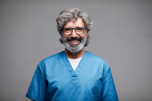 An experienced doctor with a grey beard in blue scrubs
